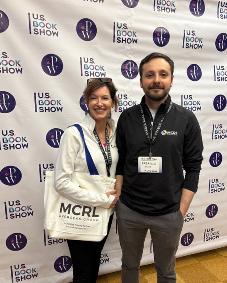 Lori and Fab standing at the 2026 U.S. Book Show with an MCRL tote bag